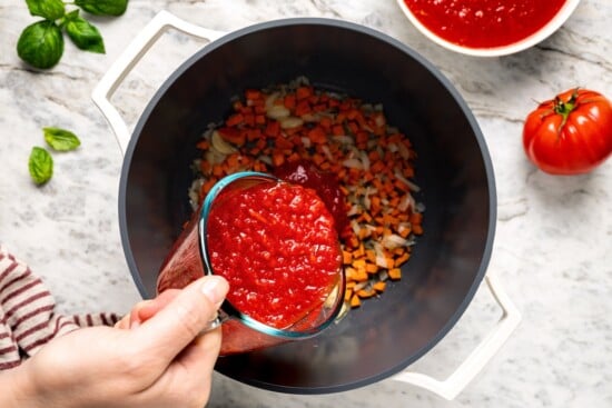 This filetto di pomodoro tastes far better than store-bought pasta sauces! You only need a few ingredients for this authentic Italian recipe. Pouring crushed tomatoes into pot with carrots and onion.