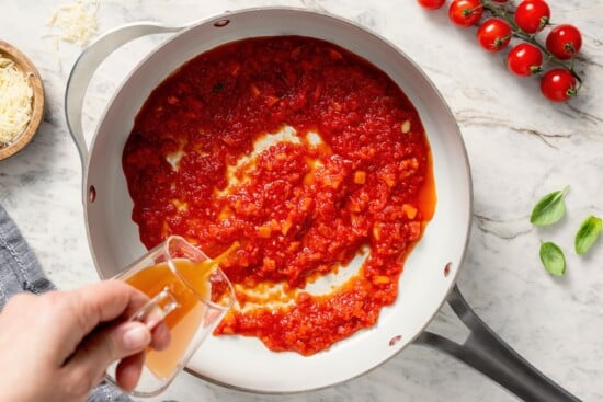 Pouring broth into skillet of sauce.