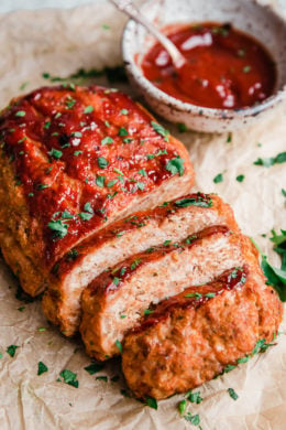 Turkey meatloaf cut into slices next to a bowl of ketchup glaze.