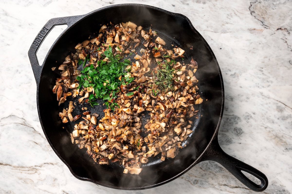 Fresh herbs added to sautéed mushrooms and shallots in a skillet.