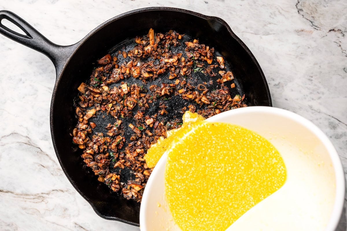 Pouring the egg mixture into a skillet with cooked mushrooms and shallots.