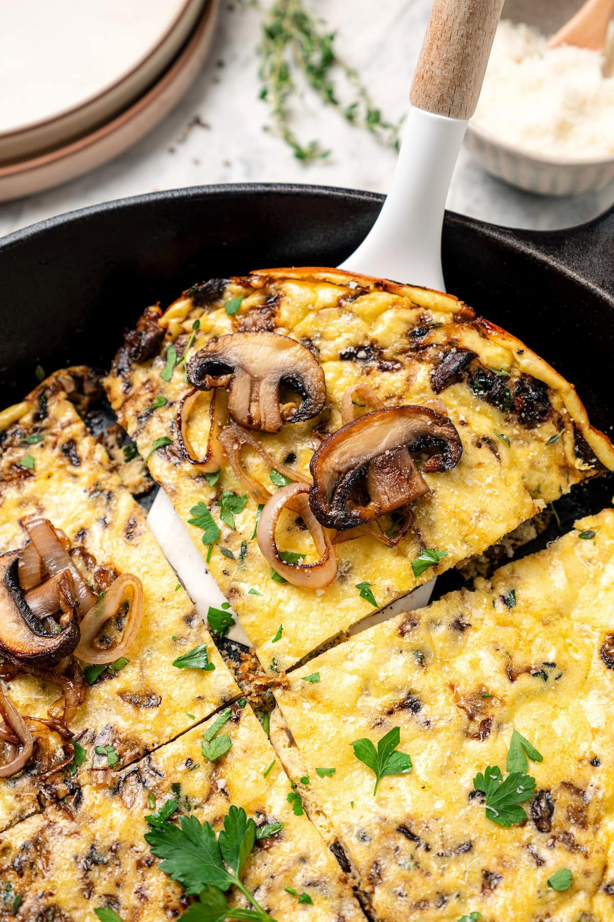 A spatula lifting a slice of mushroom frittata from a cast-iron skillet.
