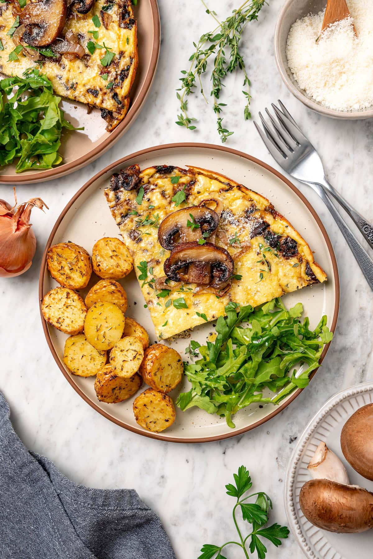 Overhead view of a slice of mushroom frittata served with crispy potatoes and fresh greens on a plate.