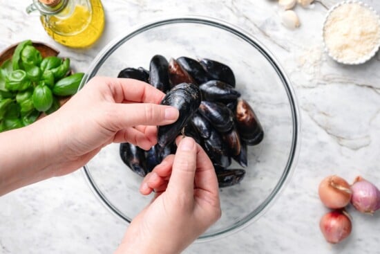 Hand holding mussel over bowl.