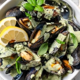 Bowl of mussels in cream sauce with fresh basil and lemon.