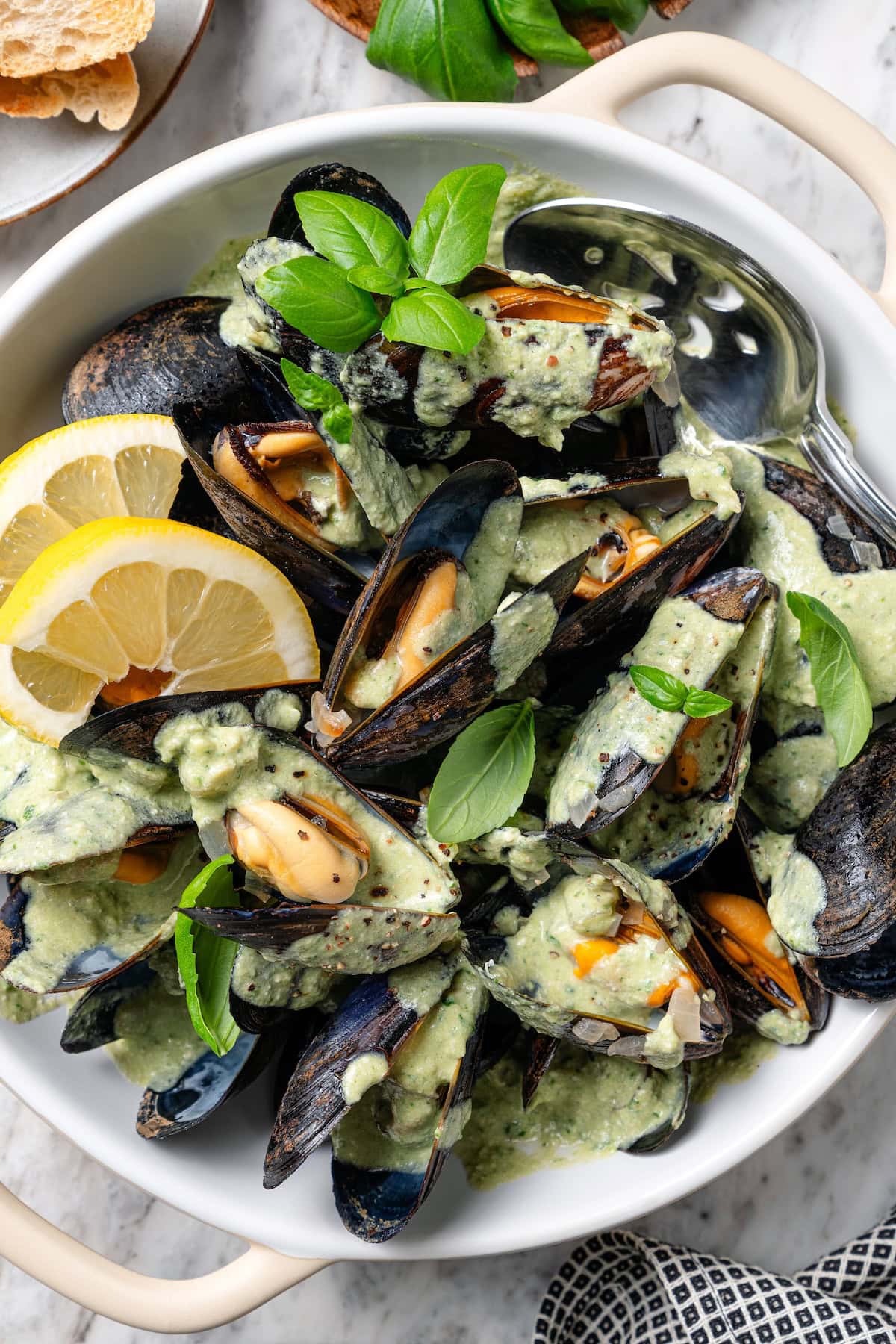 Bowl of mussels in cream sauce with fresh basil and lemon.