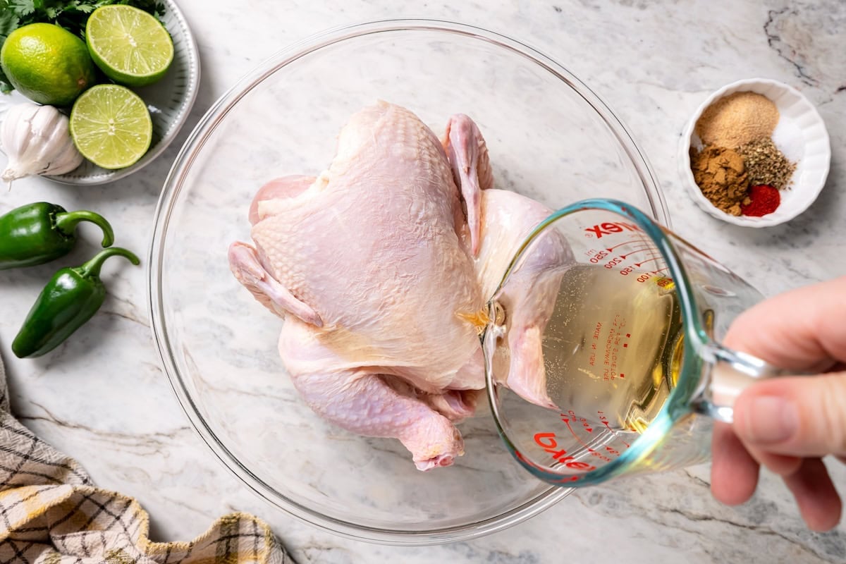 This juicy, restaurant-style Peruvian chicken is marinated overnight and oven-roasted for golden, crispy skin. Served with spicy green sauce. Pouring marinade ingredients over a whole chicken in a bowl.
