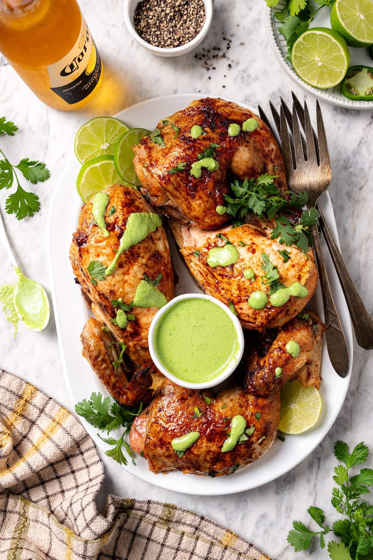 This juicy, restaurant-style Peruvian chicken is marinated overnight and oven-roasted for golden, crispy skin. Served with spicy green sauce. Overhead view of Peruvian roasted chicken served on a platter with aji verde sauce.