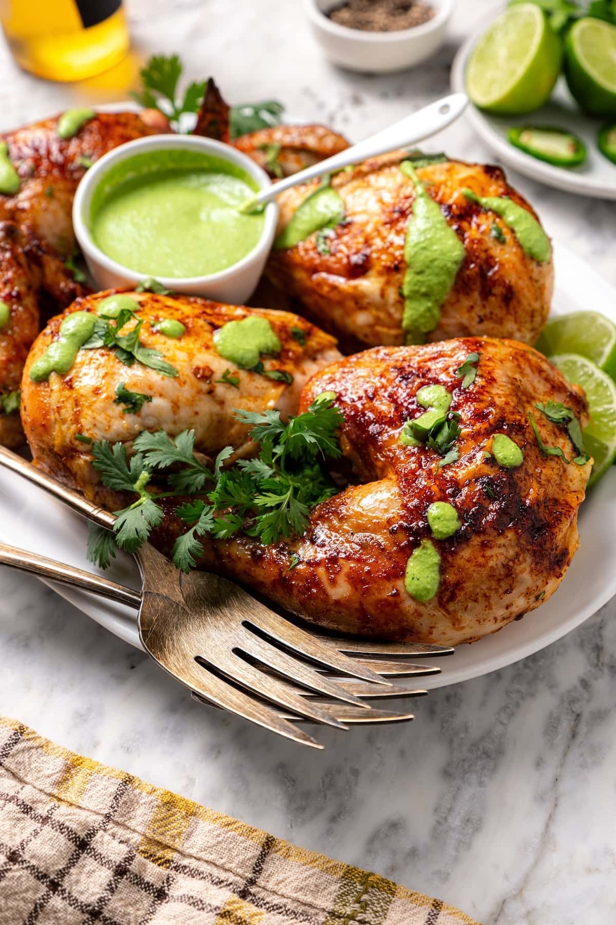 This juicy, restaurant-style Peruvian chicken is marinated overnight and oven-roasted for golden, crispy skin. Served with spicy green sauce. Peruvian roasted chicken served on a plate with aji verde sauce.