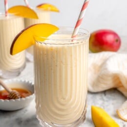 Mango lassi in glass with straw and mango slice on rim for garnish
