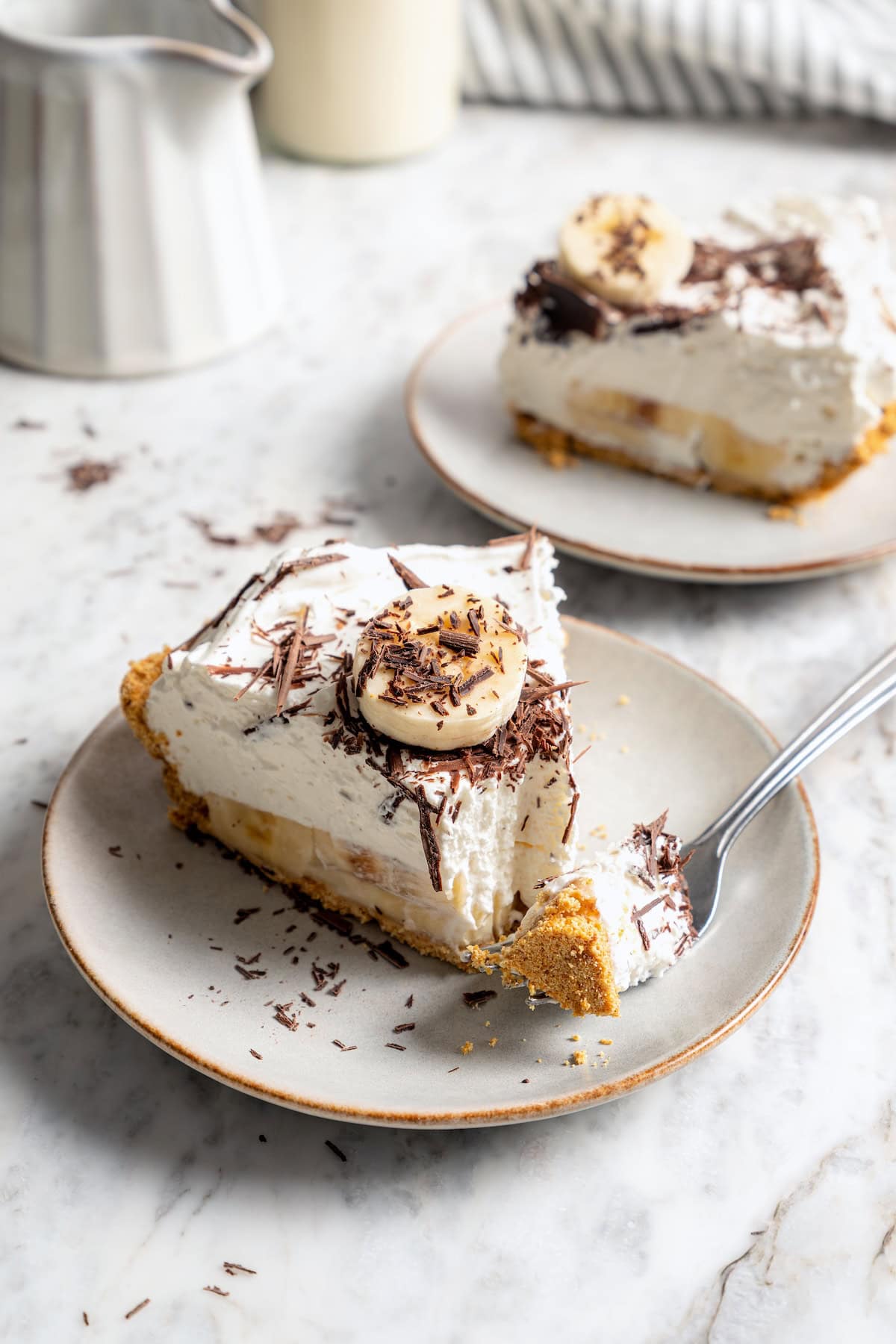 Slice of banana cream pie on plate with tip of pie on fork.