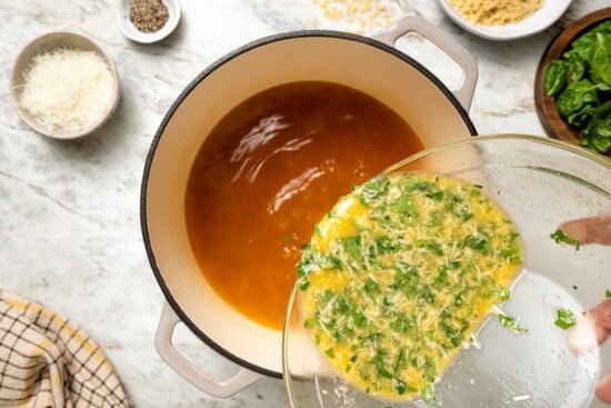 Pouring egg mixture into pot of broth.