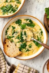 Spoon in bowl of stracciatella soup with orzo and spinach.