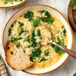 Spoon in bowl of stracciatella soup with orzo and spinach.