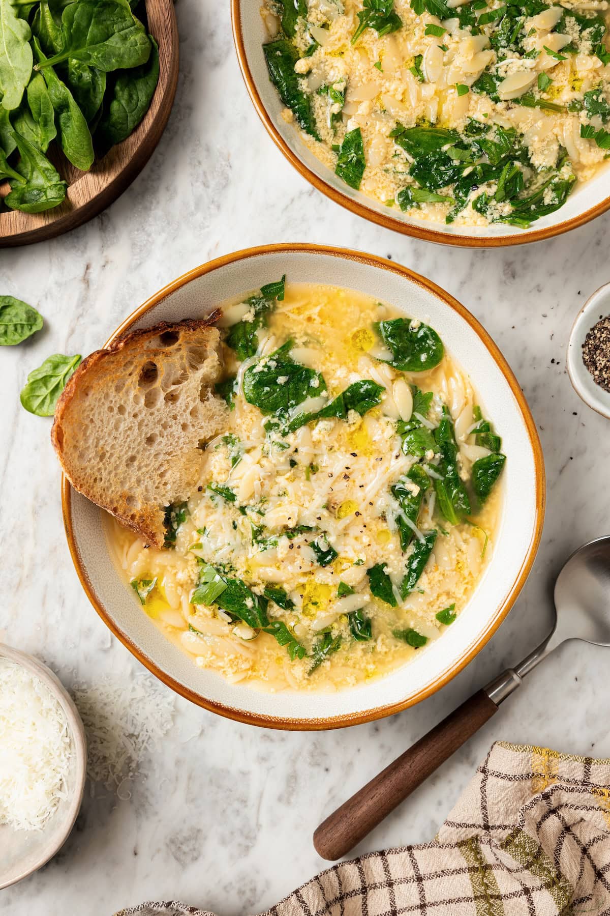 Two bowls of stracciatella soup with orzo and spinach.