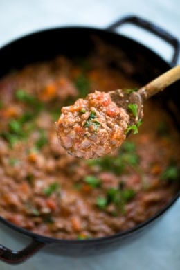 A spoonful of bolognese sauce held over a pot of sauce.