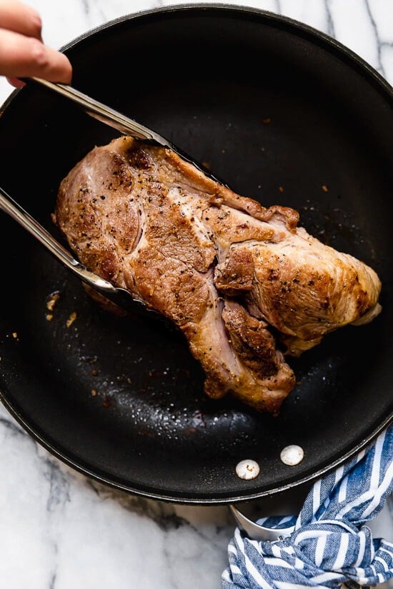 Slow cooked until tender then crisped in the oven, these pork carnitas are practically effortless to make and perfect for meal prep. Tongs grabbing pork shoulder in skillet.