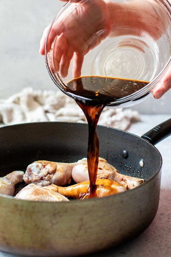 Pouring soy sauce and vineger over chicken drumsticks.