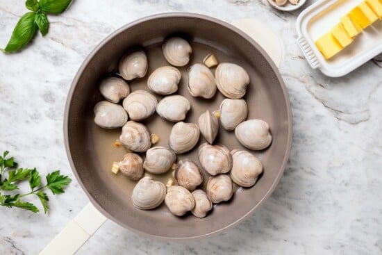 Clams in skillet with cooking liquid.