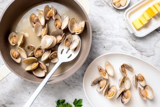 Slotted spoon removing steamed clams from skillet.