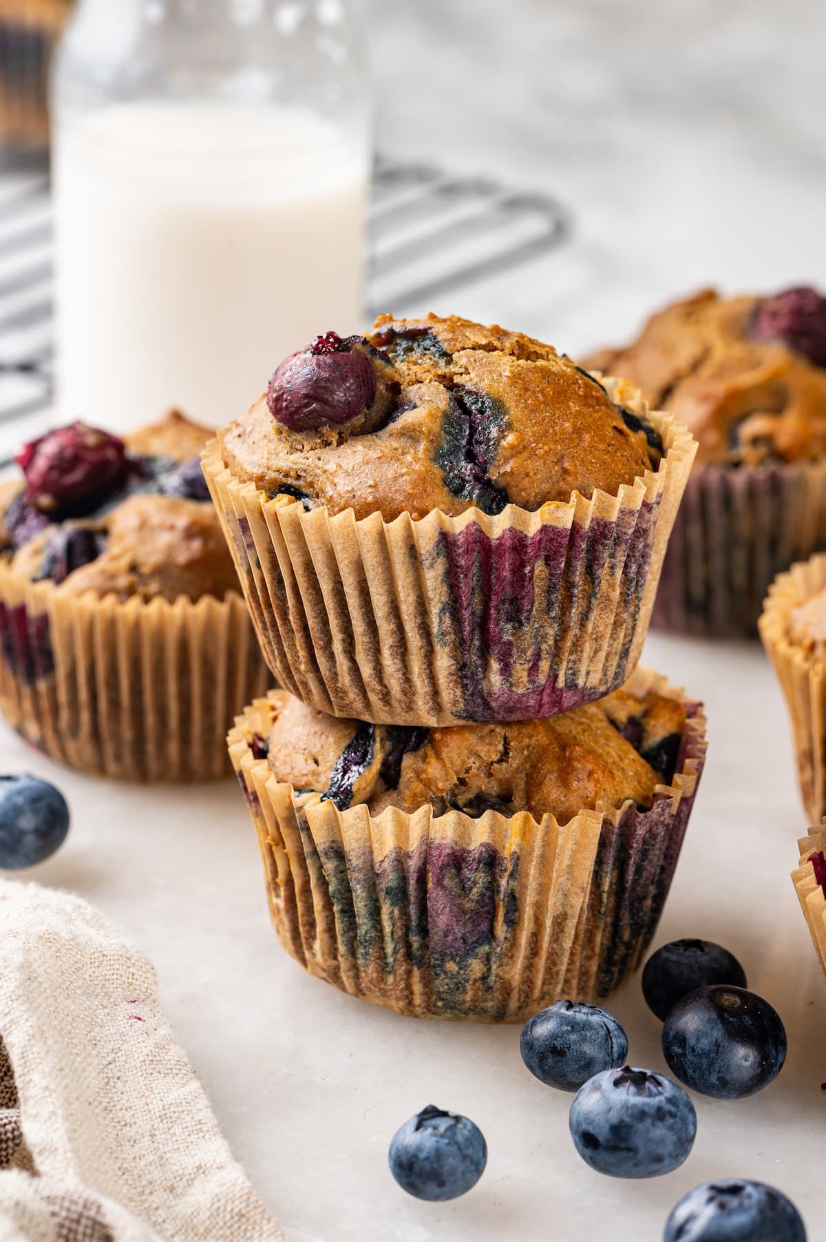 Stack of 2 blueberry muffins with additional muffins and jug of milk in background