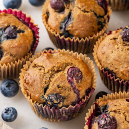 Whole wheat blueberry muffins on counter with fresh blueberries