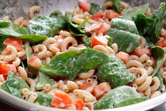 A bowl of elbow macaroni, baby spinach, and diced tomatoes coated with creamy dressing