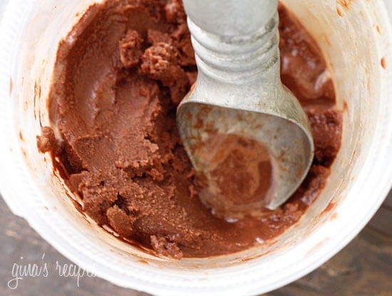 An ice cream scooper inside a bucket of chocolate sorbet.