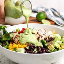 Pouring avocado cilantro lime dressing over salad in bowl.