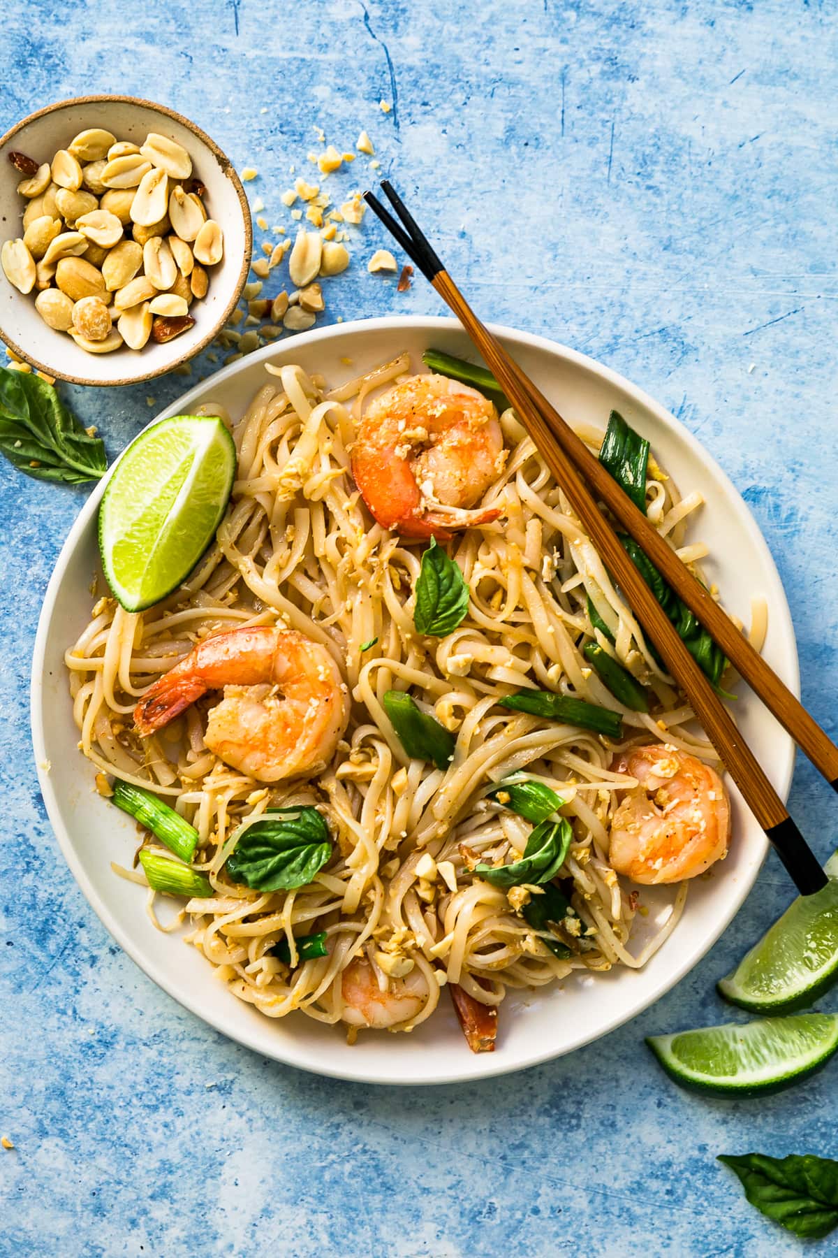 Overhead view of shrimp Pad Thai in bowl with peanuts, lime wedges, and basil for garnish