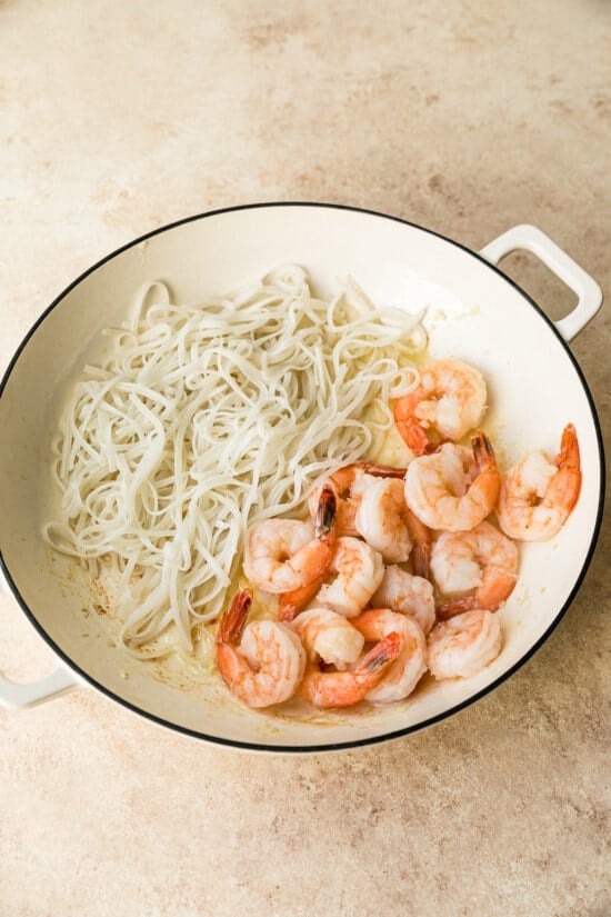 Noodles on one side of wok with cooked shrimp on other side
