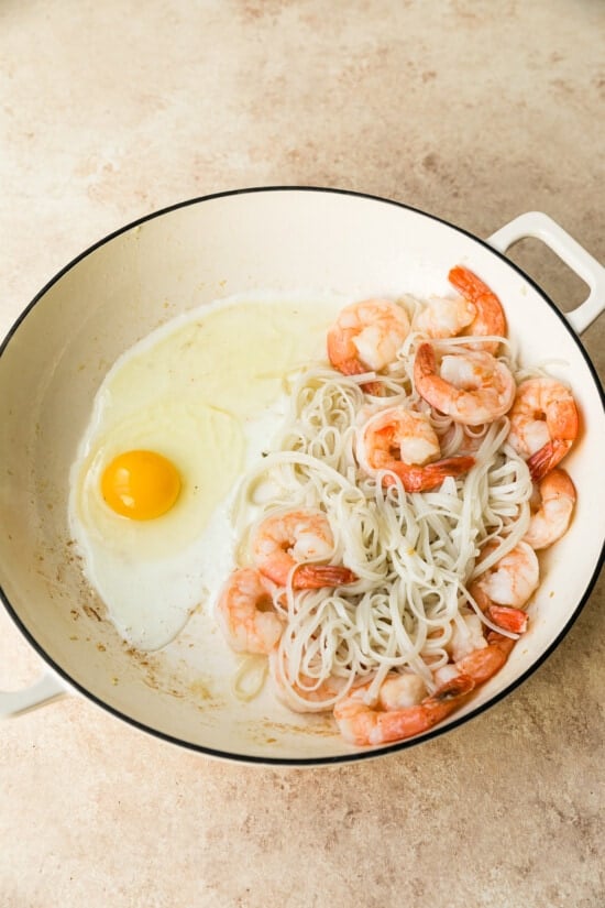 Egg cracked into wok with shrimp and noodles