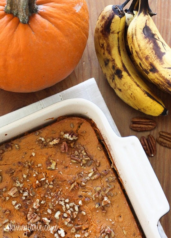 A casserole dish with pumpkin baked oatmeal next to a pie pumpkin and bunch of ripe bananas