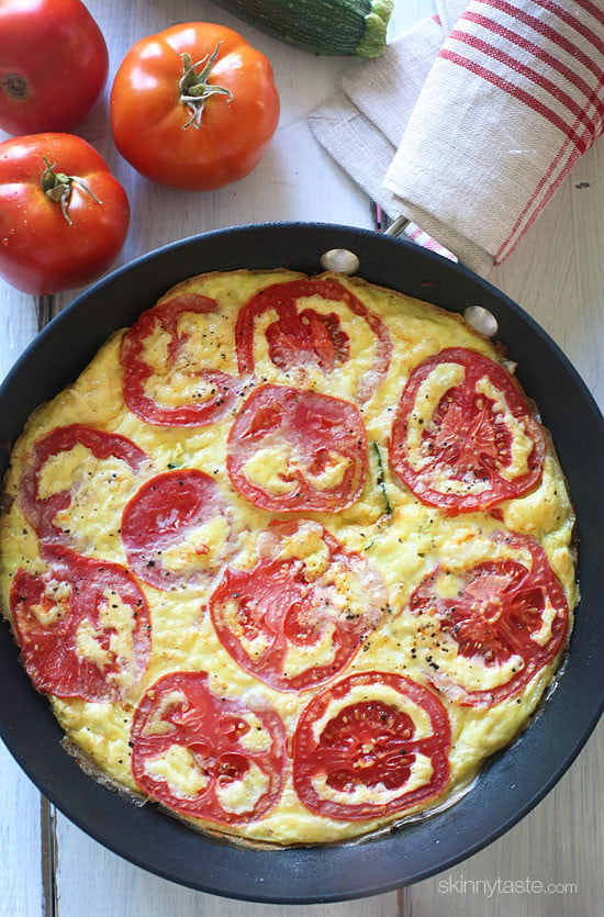 Frittata in a skillet with sliced tomatoes on top.