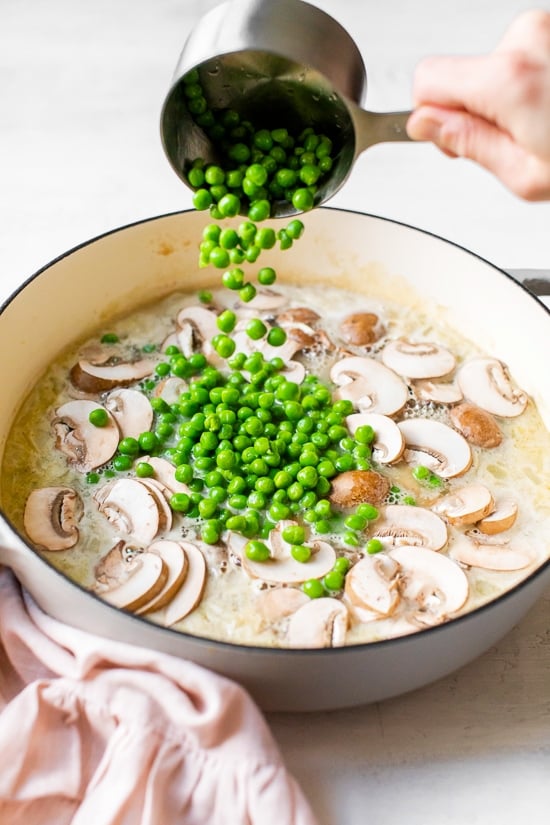 adding peas to a pot with mushrooms