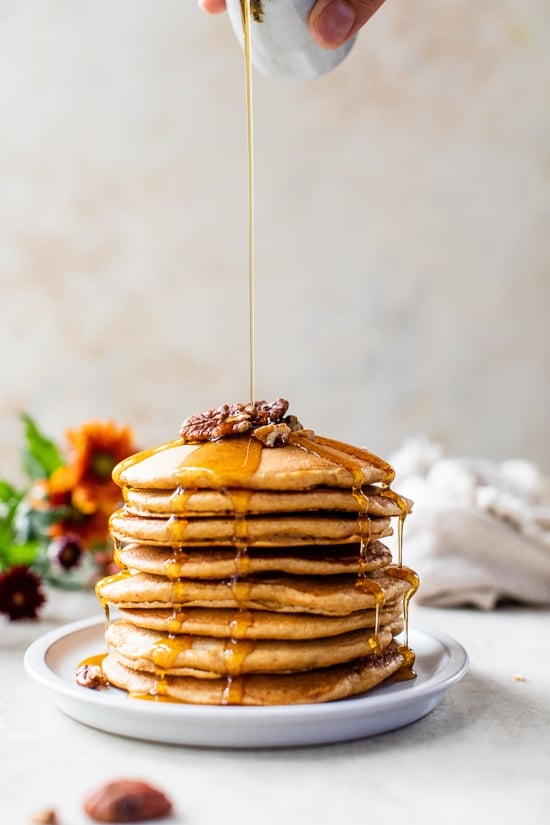 Syrup being poured over a stack of pumpkin pecan pancakes