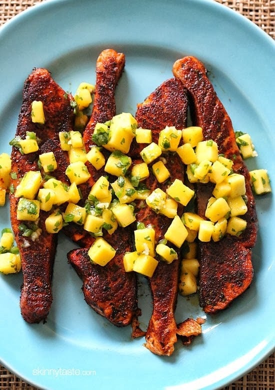 Blackened salmon fillets on a plate topped with mango salsa