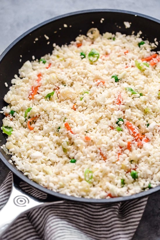 This low-carb cauliflower fried rice recipe is quick, flavorful and a great way to enjoy your favorite takeout-style dish in a lighter way! Cauliflower rice added to skillet with vegetables.