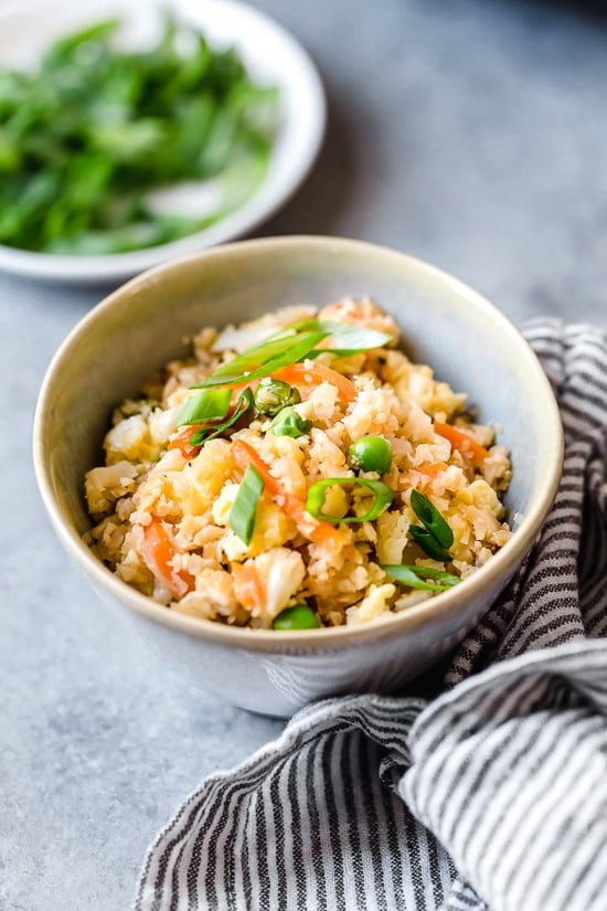 This low-carb cauliflower fried rice recipe is quick, flavorful and a great way to enjoy your favorite takeout-style dish in a lighter way! Bowl of cauliflower fried rice with scallions.
