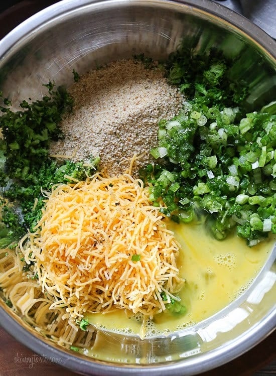 A mixing bowl with chopped broccoli, breadcrumbs, sliced scallions, grated cheese and egg