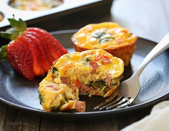 A strawberry and two loaded mini quiches cut in half with a fork on a plate.