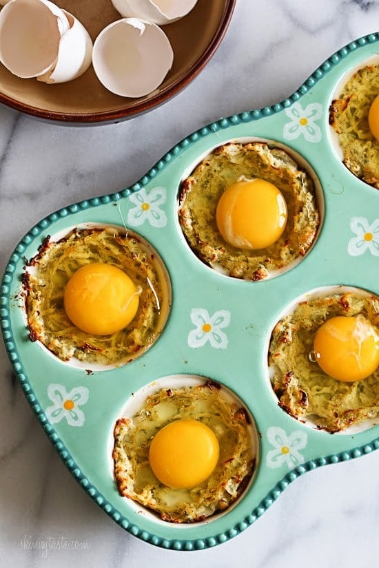 A muffin pan lined with spaghetti squash mixture and a raw egg on top of each