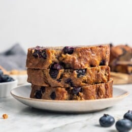 Stack of 3 blueberry banana bread slices on plate.