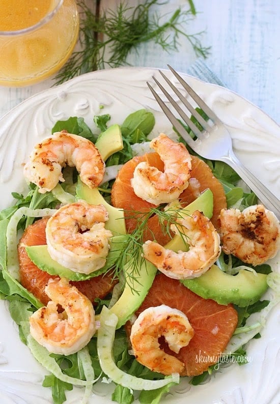 A bowl of greens topped with sliced oranges, sliced avocado, sliced fennel and grilled shrimp.