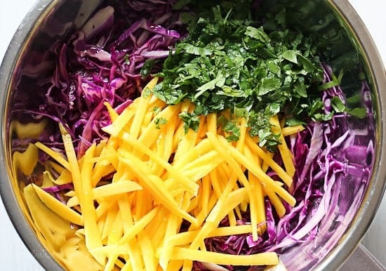 A mixing bowl with shredded red cabbage, julienned mango, and chopped cilantro
