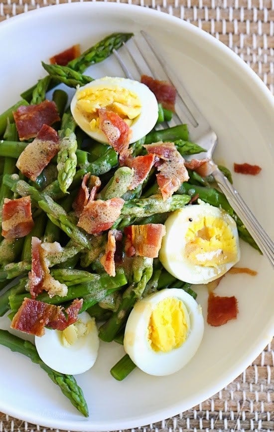 A bowl of cut asparagus pieces topped with hard-boiled eggs and chopped bacon.