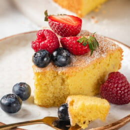 Almond cake on plate with fresh berries, with tip of cake on fork