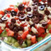 This Greek 7 Layer Dip is layered with hummus, yogurt, cucumbers, tomatoes, feta and olives. Grab a chip and serve this at your next party!