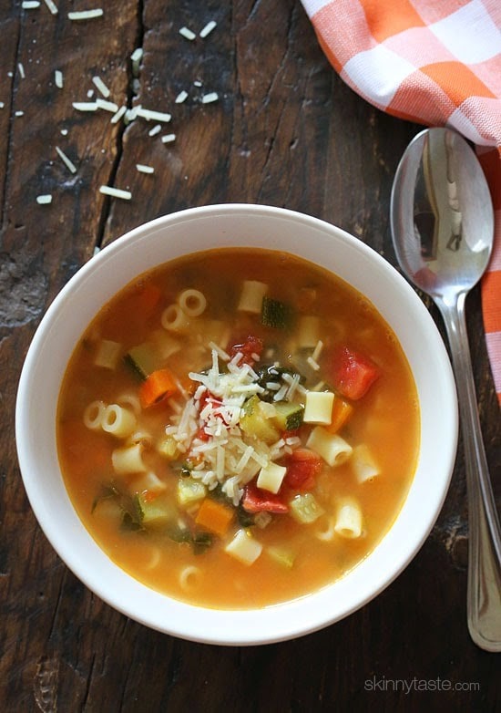 A bowl of minestrone soup with tomato-based broth, vegetables, short tubular pasta, and shredded parmesan cheese.