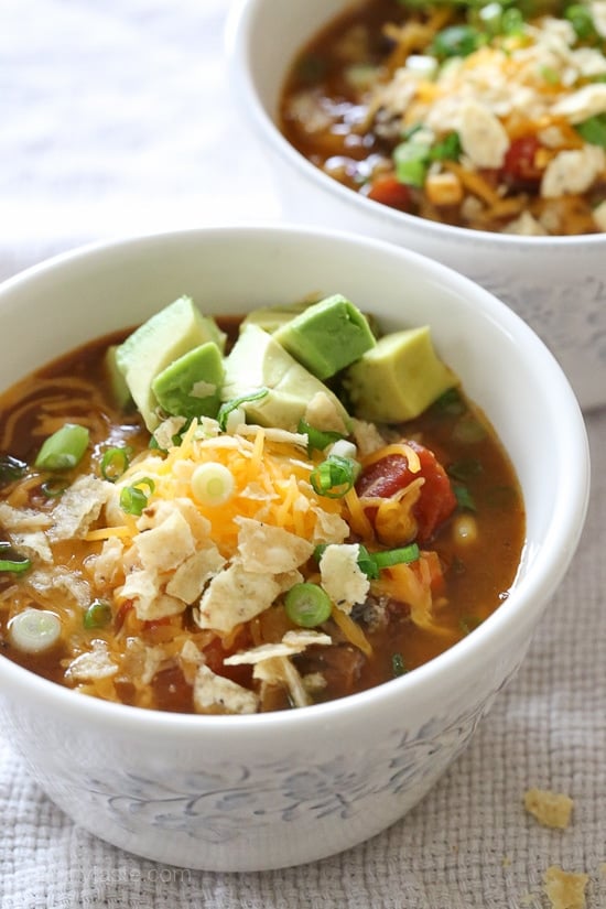 A bowl of pumpkin chili topped with shredded cheese and avocado